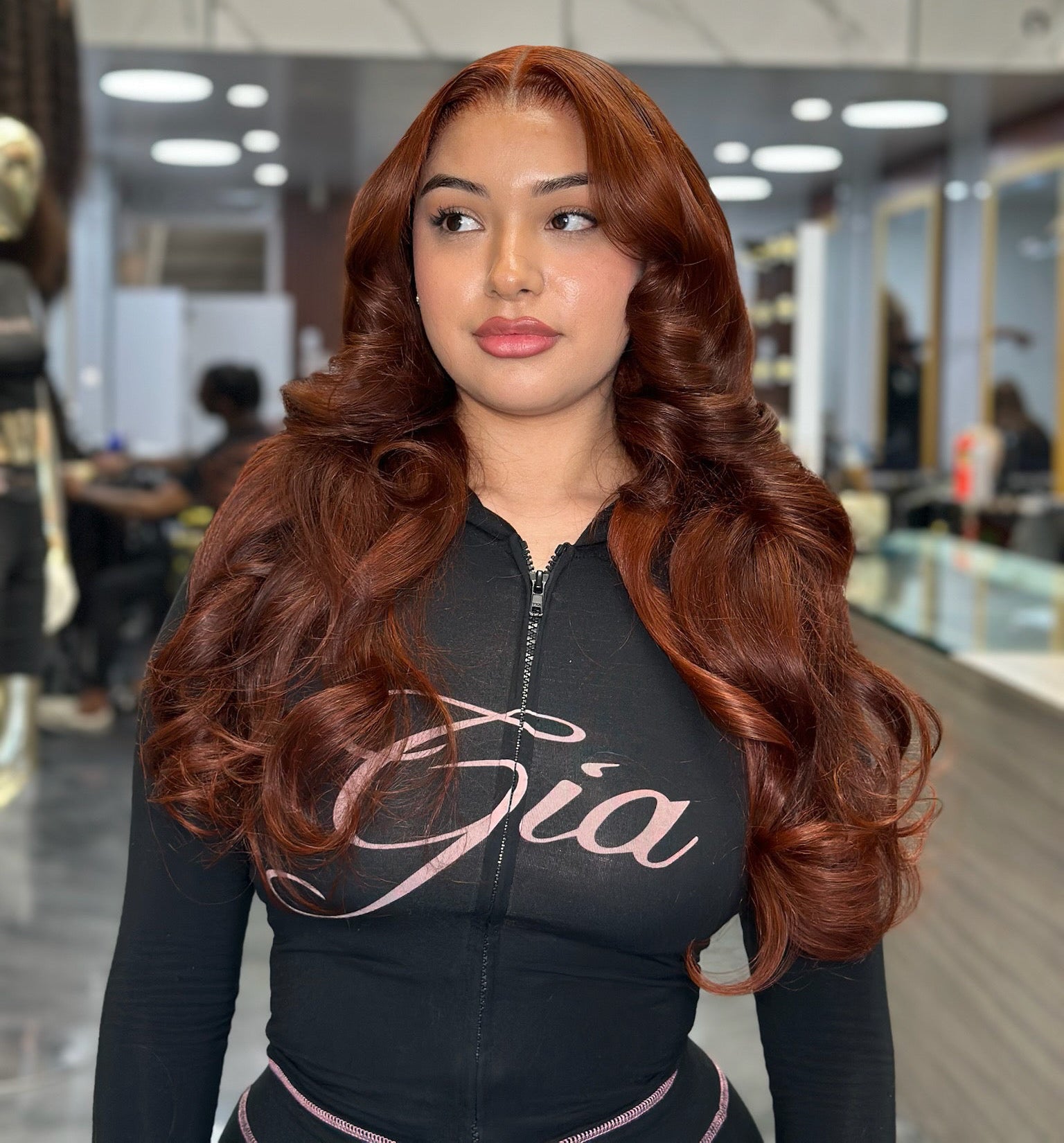 Women's black zip hoodie with pink cursive logo; long auburn wavy hair