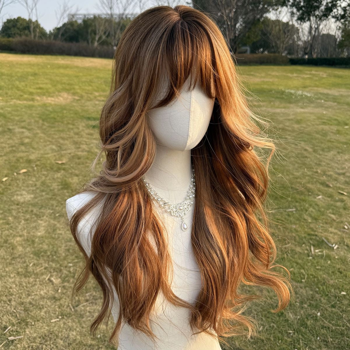 Long wavy auburn-brown wig with bangs and lighter highlights, viewed from back-left.