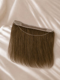 Hair topper piece with transparent lace base and long straight blonde-brown strands.