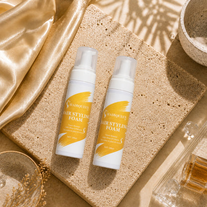 Two HQLA hair styling foam pump bottles on a speckled sponge with gold fabric