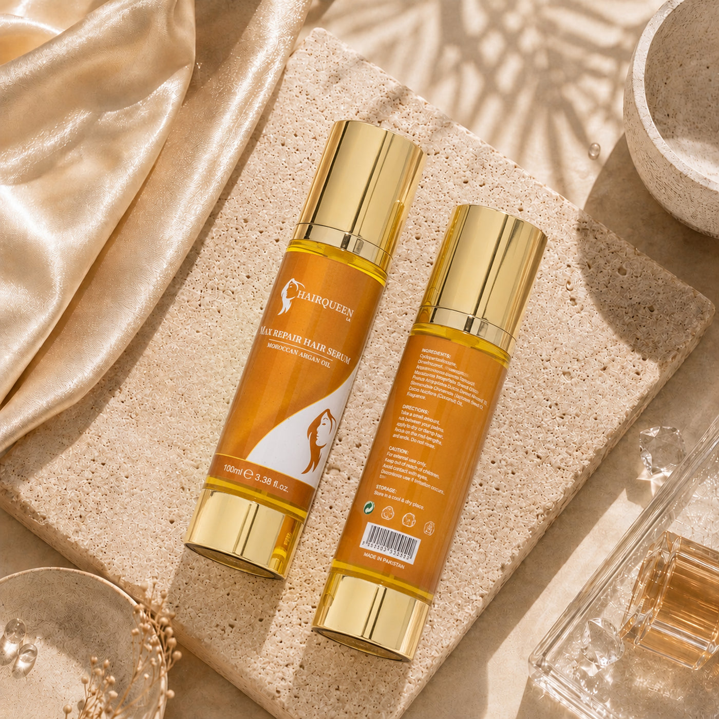 Hair repair serum duo, amber-orange bottles with gold caps on a stone tray