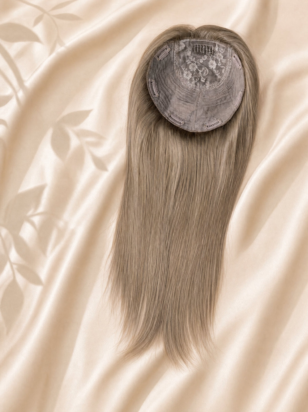 Circular silk base topper with embedded gray net and long straight hair.