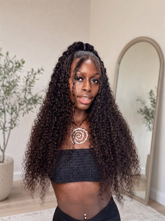 Long deep-wave curly wig with dark hair, natural hairline and center part.