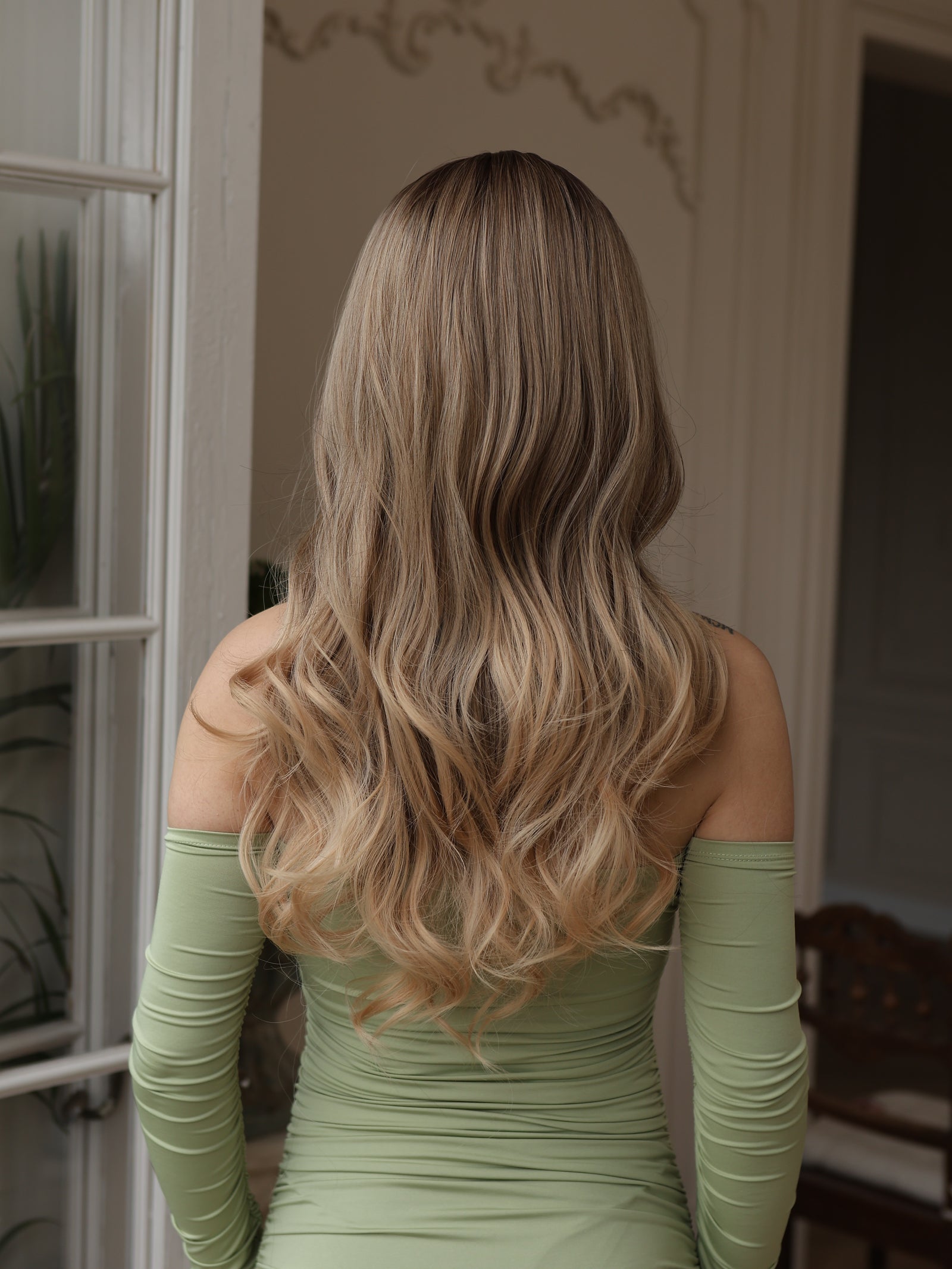 Long wavy wig back view with dark roots, light brown hair and blonde icy highlights
