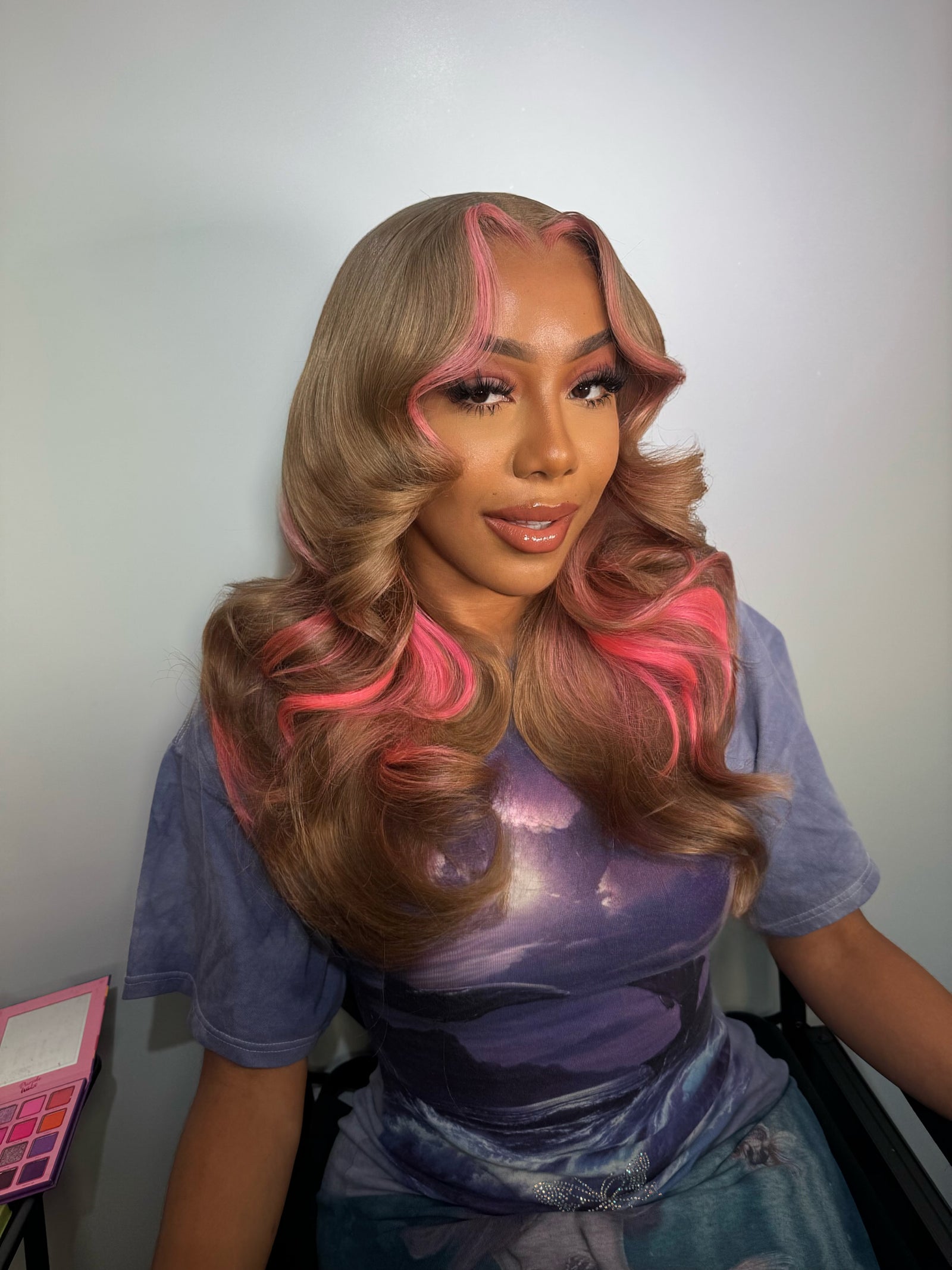 Long wavy lace wig with blonde-brown curls and vivid pink highlights, side-parted.