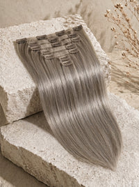 Ash gray straight-to-wavy clip-in hair extensions shown on a swatch with clips