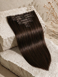 Folded dark hair extension weft with visible clips on a light fabric backing