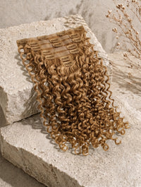 Curly golden-brown clip-in hair extensions weft with comb clips attached.