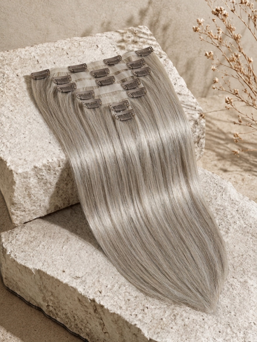 Seamless clip-in extensions, long straight ash-blonde hair bundle with visible weft clips.