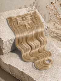 Seamless clip-in extensions, long wavy light blonde hair bundle with visible weft clips.