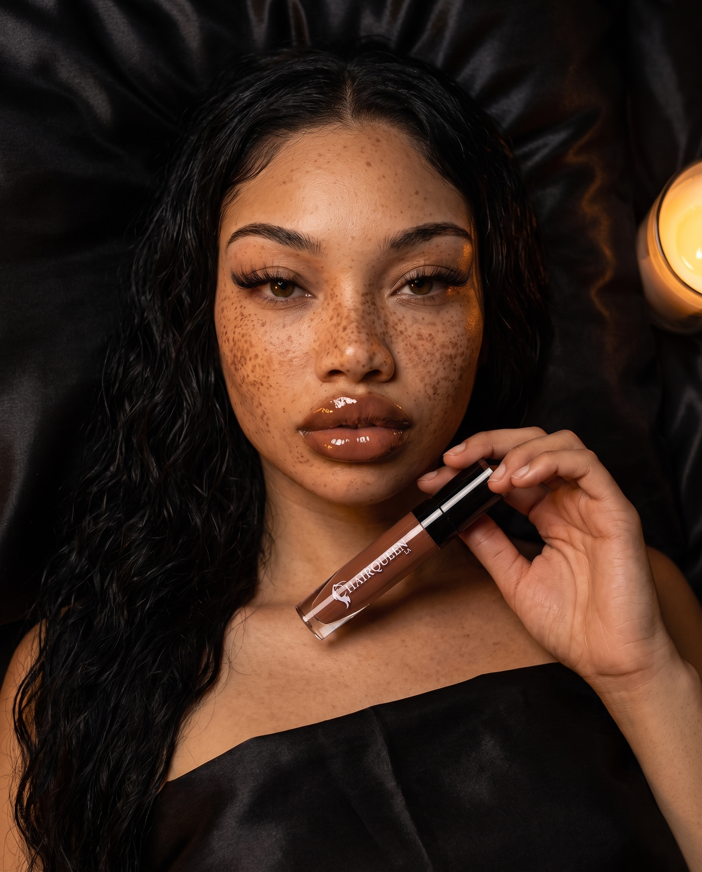 Lip gloss being applied to glossy nude-brown lips by model, wand in hand