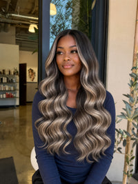 Highlighted long wavy hair on a woman, center-parted style in dark and blonde tones