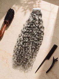 Curly tape-in hair extensions in cool ash blonde, dense ringlet curls with adhesive strip.