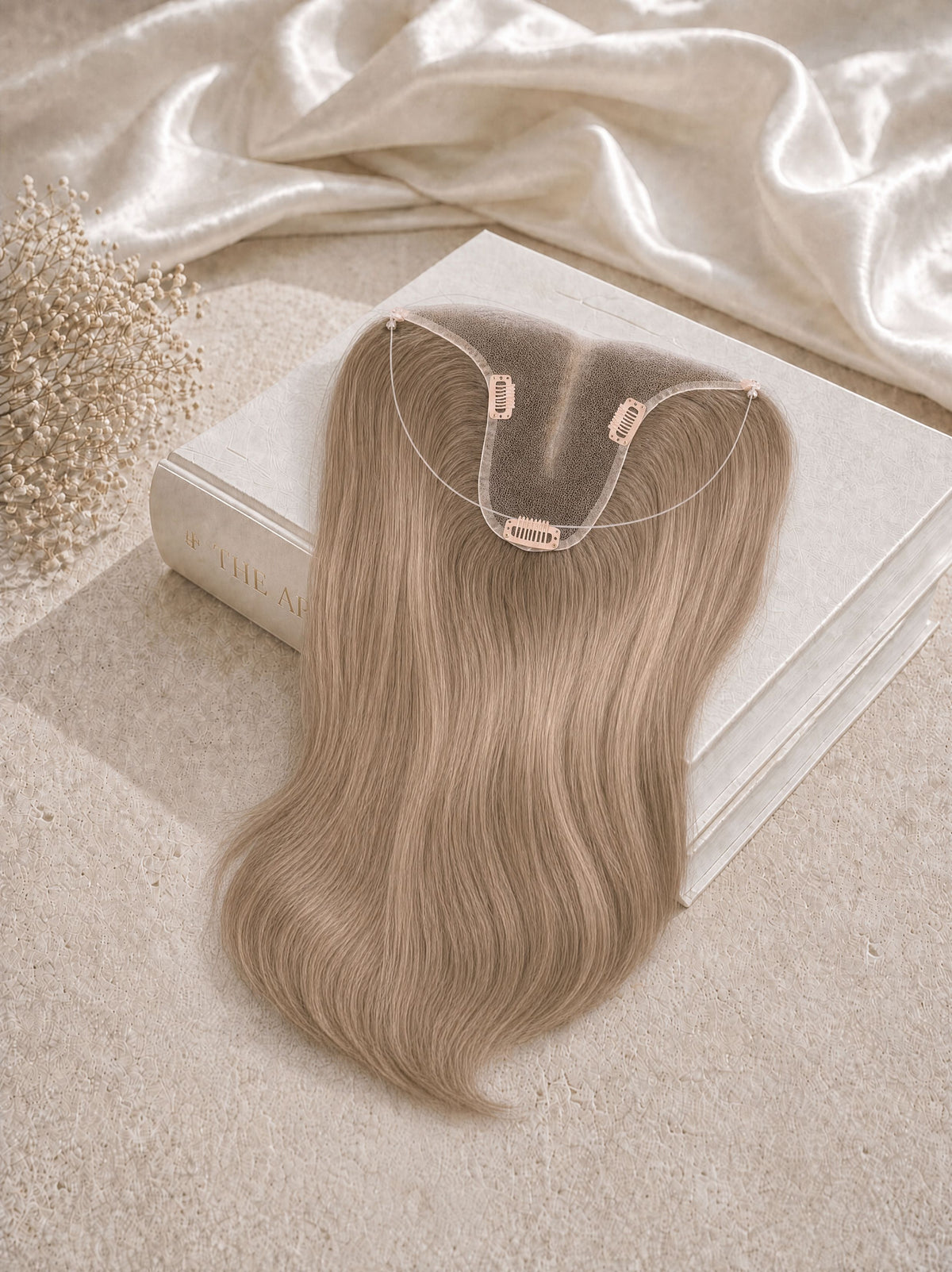 Light blonde hair topper with U-shaped clip base laid on a satin cloth