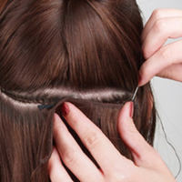Hair extension sew-in installation, hands tucking a dark weft under the hair