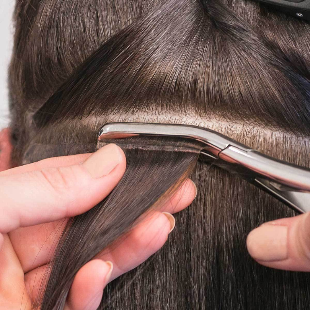 Tape-in hair extension install class demonstrating hands securing a weft to hair